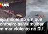 Um bombeiro se lança em um mar agitado, enfrentando rochas, com o objetivo de resgatar uma mulher em Niterói, no estado do Rio de Janeiro